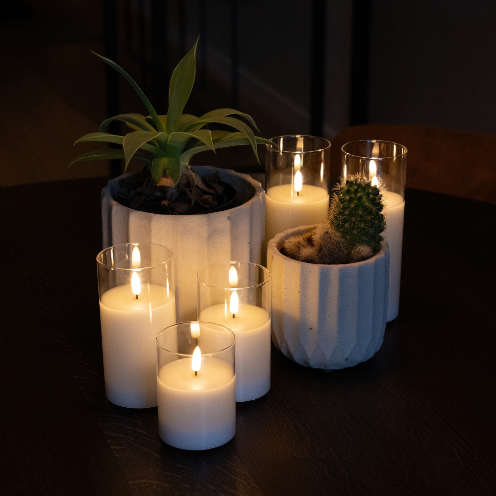 Akaro kaarsen in glas rond twee planten op een donkere ronde tafel