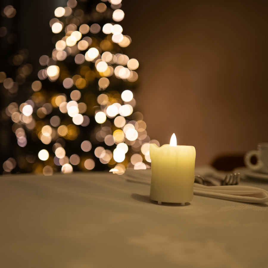 Een Akaro kaars op een gedekte tafel, met een verlichte kerstboom onscherp erachter