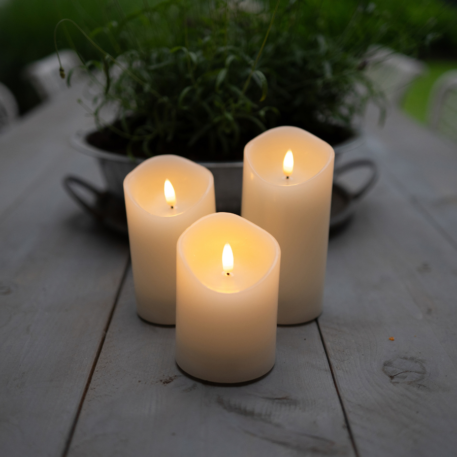 Drie Akaro LED kaarsen op een houten tuintafel bij een pot met kruiden