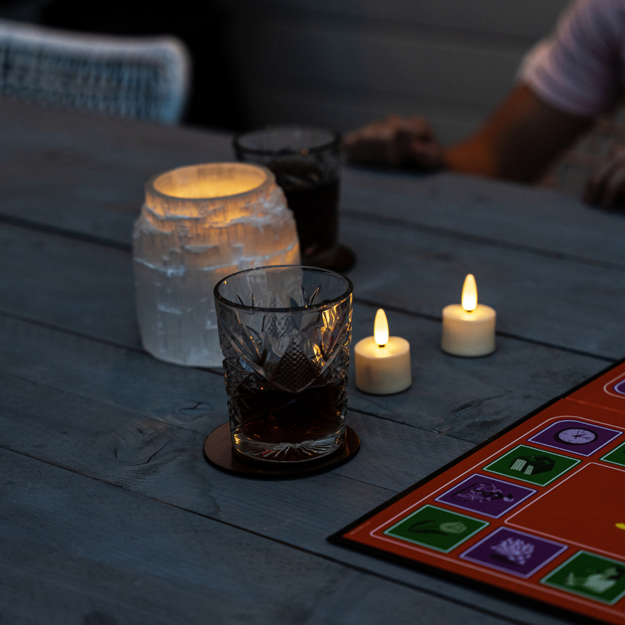 Twee Akaro waxinelichtjes op een houten tafel bij een bordspel en een glas